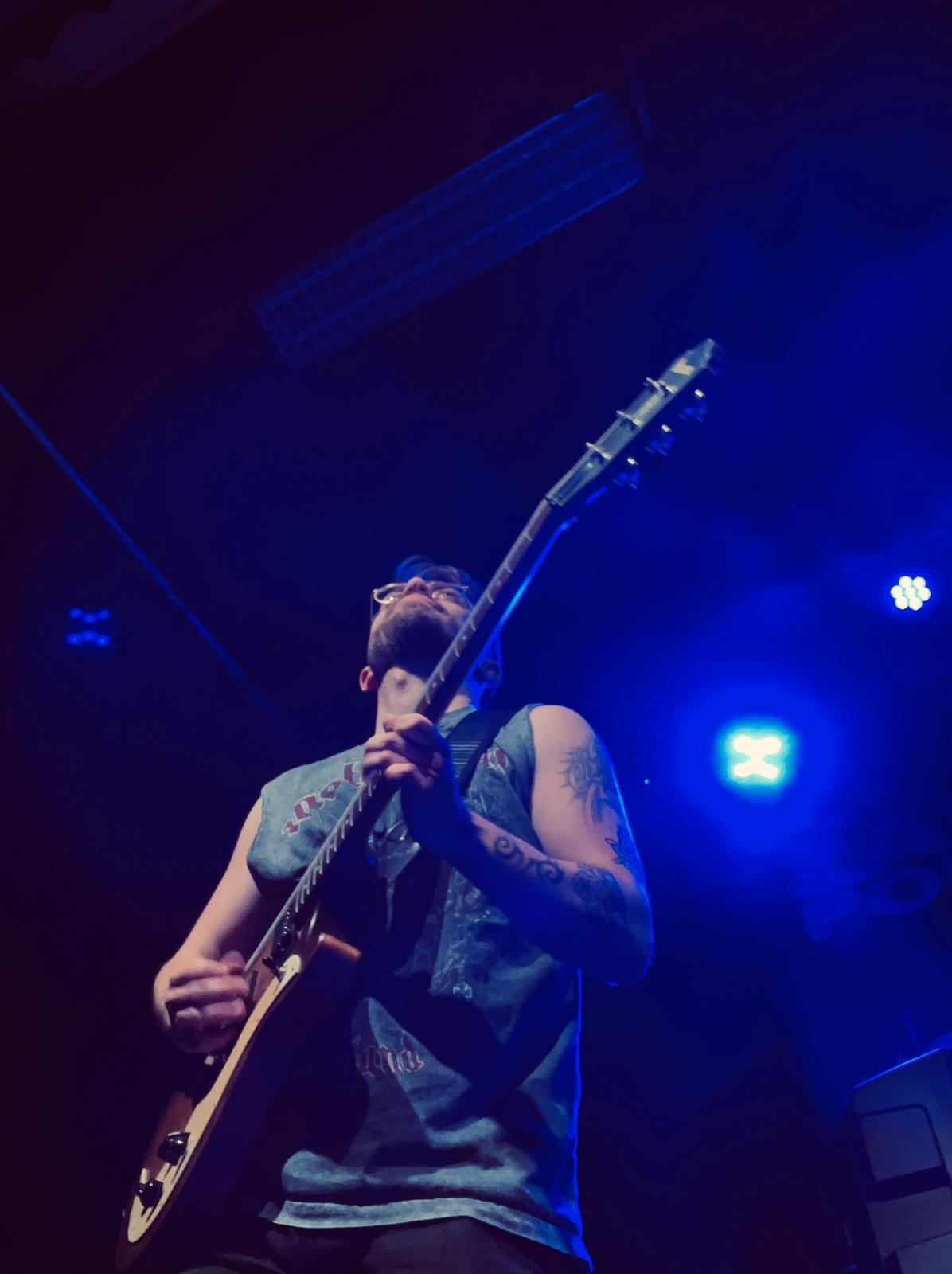 Bas van Hal speelt gitaar live op een podium met blauwe belichting